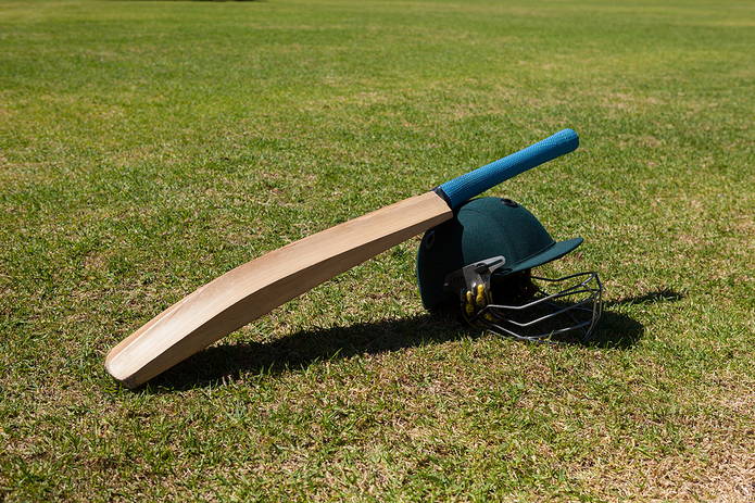 Cricket Bat Leaning on Green Helmet